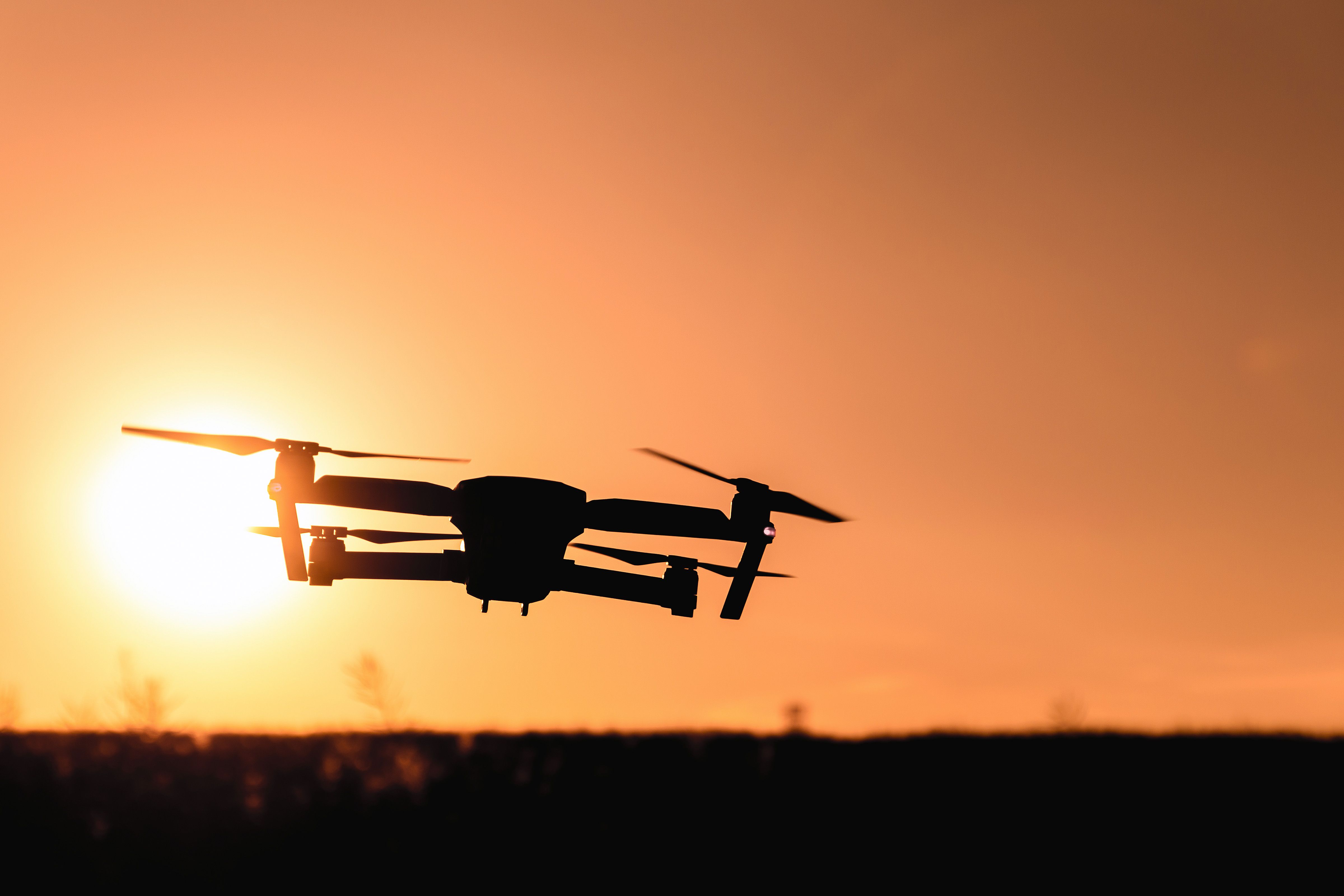 Dron v siluetě proti oranžové obloze při západu slunce